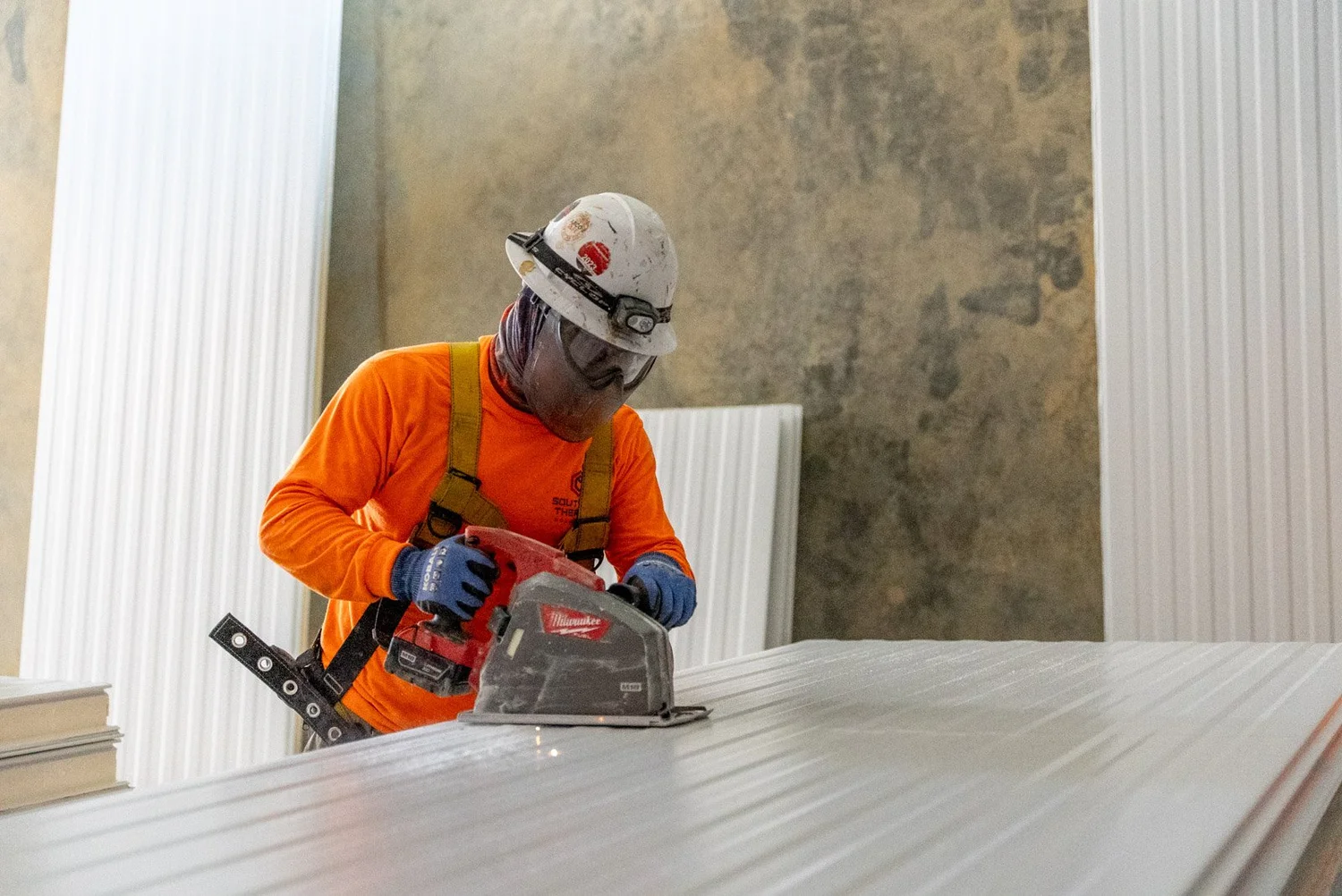 Construction worker in safety gear using a power saw on a panel.