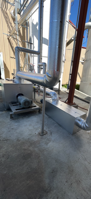 Industrial piping system with metal pipes, a motor, and a metal enclosure on a concrete floor outdoors.