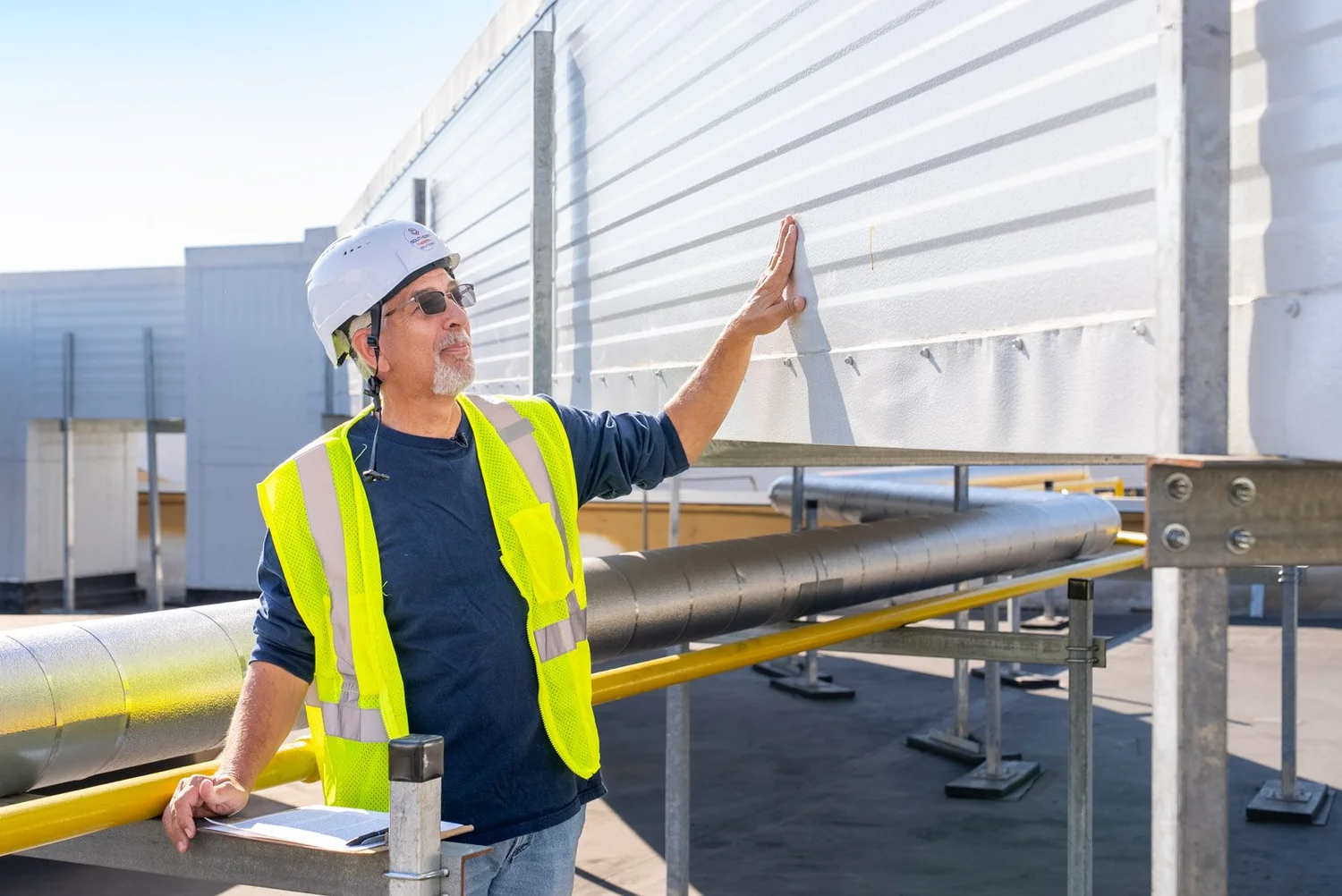 Crew member in a hard hat touching the side of a rooftop insulated metal panel duct