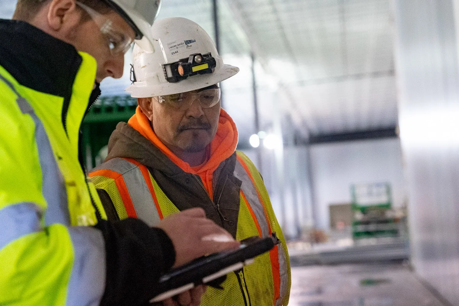 Two crew members in hard hats reviewing a tablet on the job site