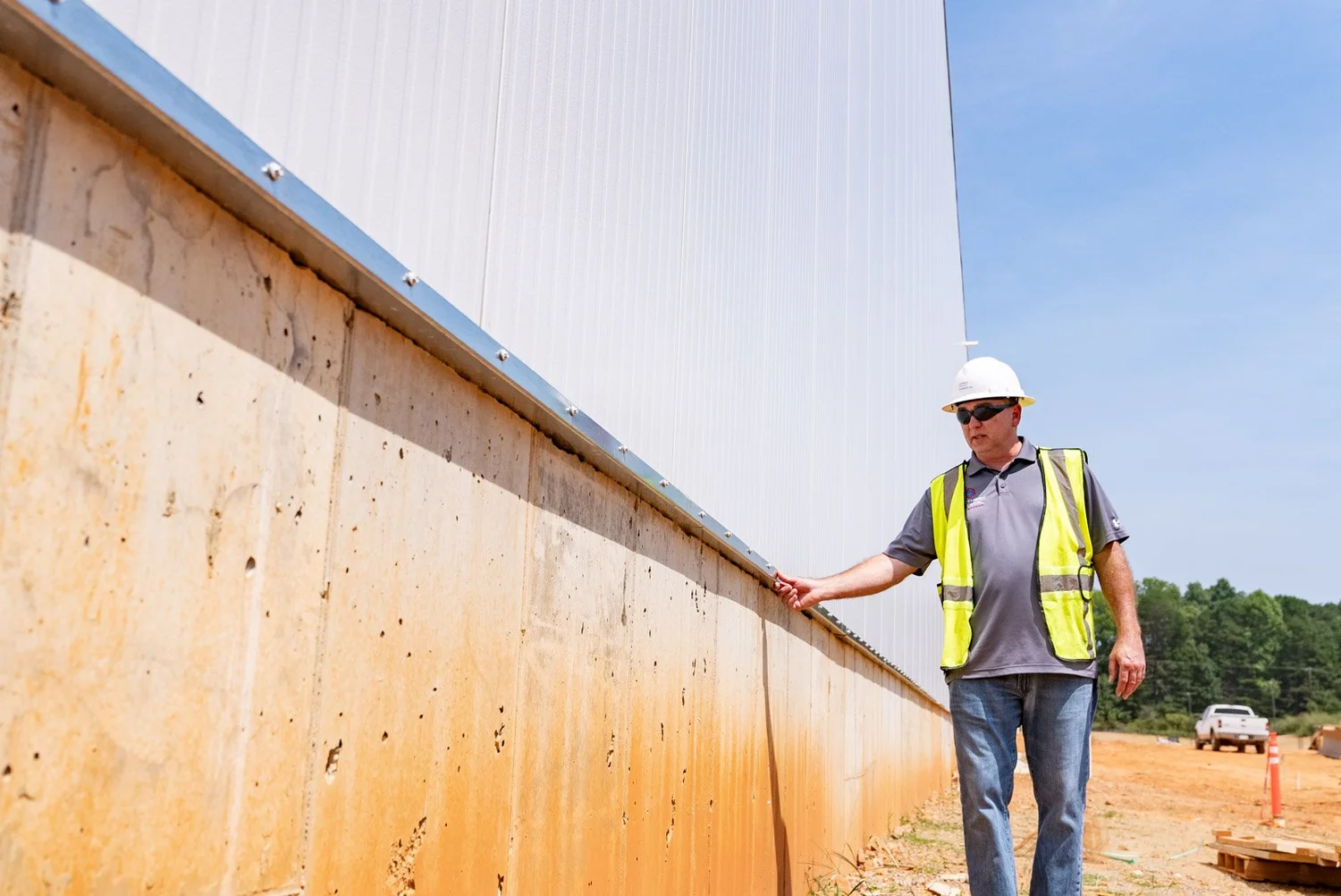 Crew member in a safety vest inspecting the base of a tall exterior insulated panel wall