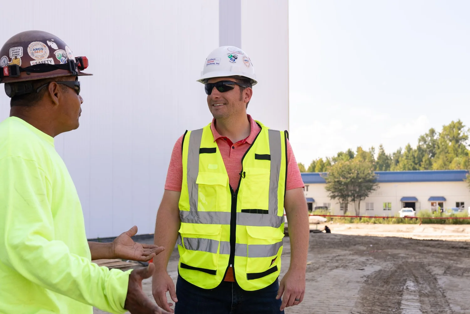 Two crew members in hard hats talking outside a new insulated panel building