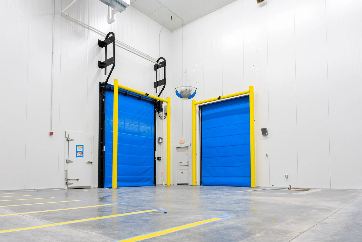 Two blue insulated high-speed doors with yellow bollards in a cold storage building