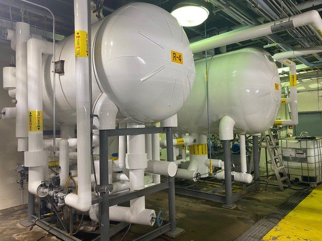 Industrial refrigeration or HVAC equipment with large white tanks labeled R-4, connected by white pipes in a mechanical room.