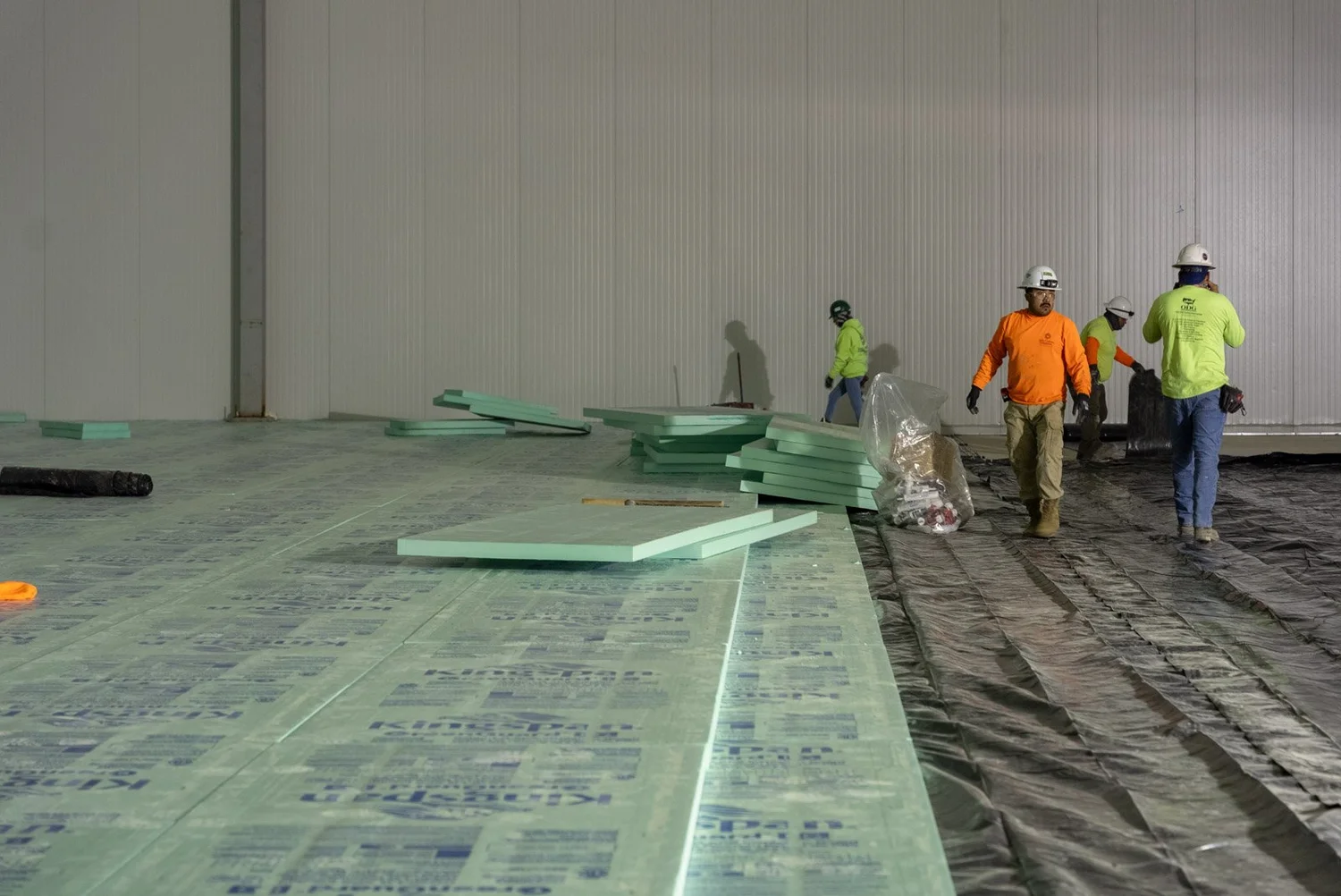Crew laying rows of under-floor insulation boards inside a cold storage building