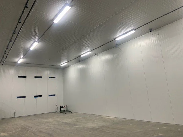 Empty industrial or storage space with white walls, concrete floor, and ceiling with fluorescent lights.