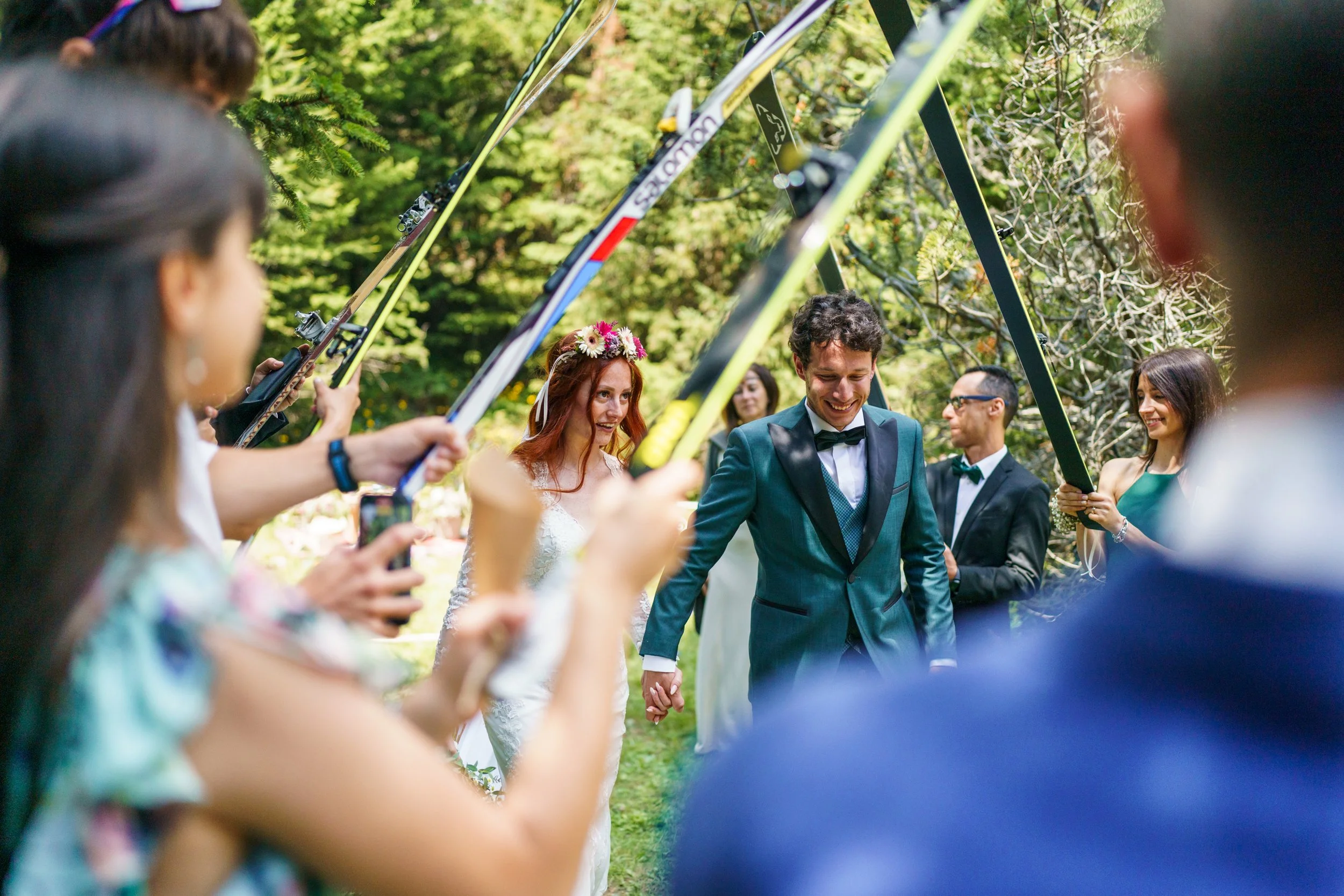 Una coppia di sposi cammina sotto un arco di sci tenuti da persone durante una cerimonia all'aperto.