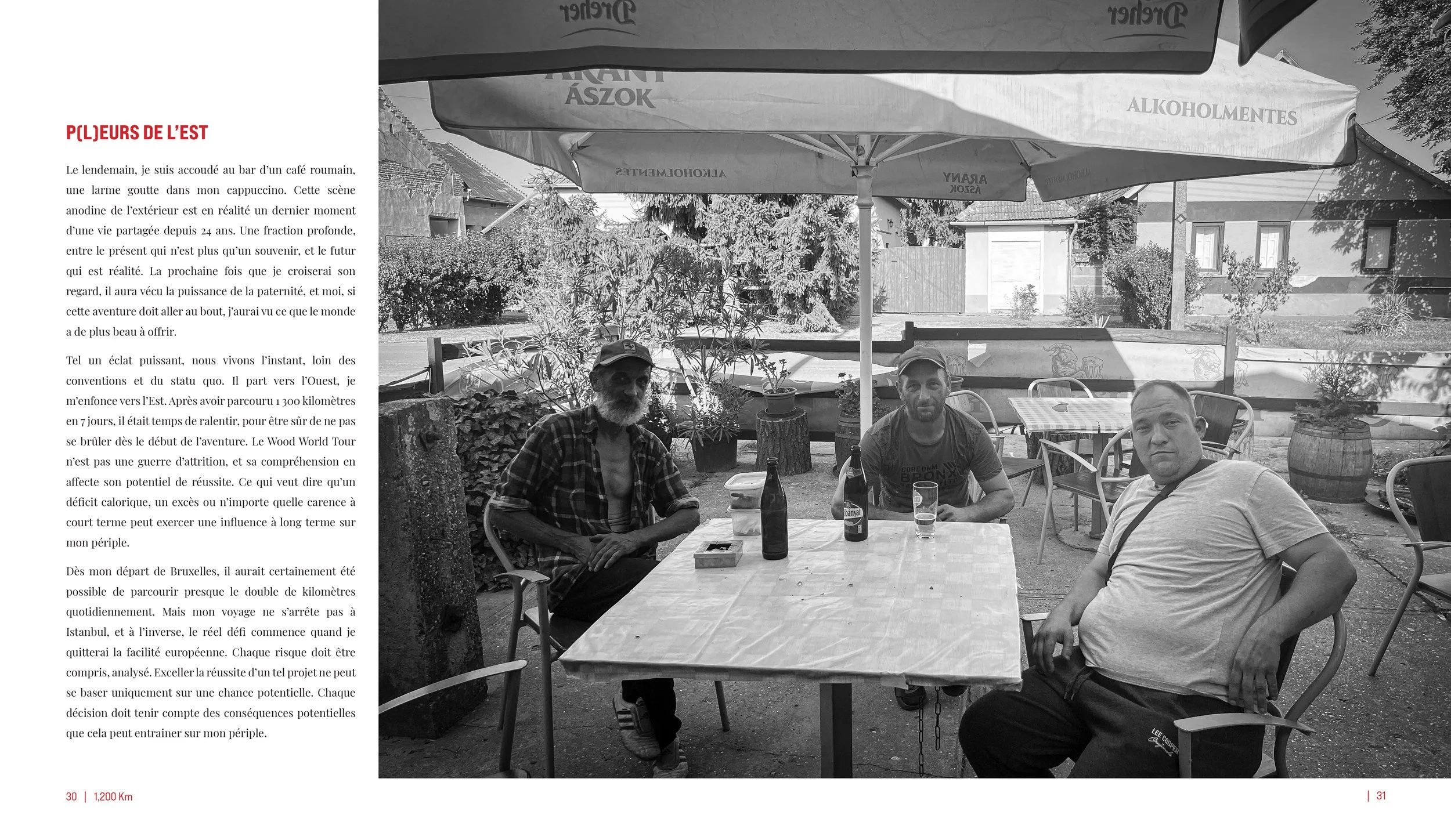 A black and white image showing three men sitting at a table outdoors under a large umbrella, with potted plants and trees in the background, in a garden or patio setting.
