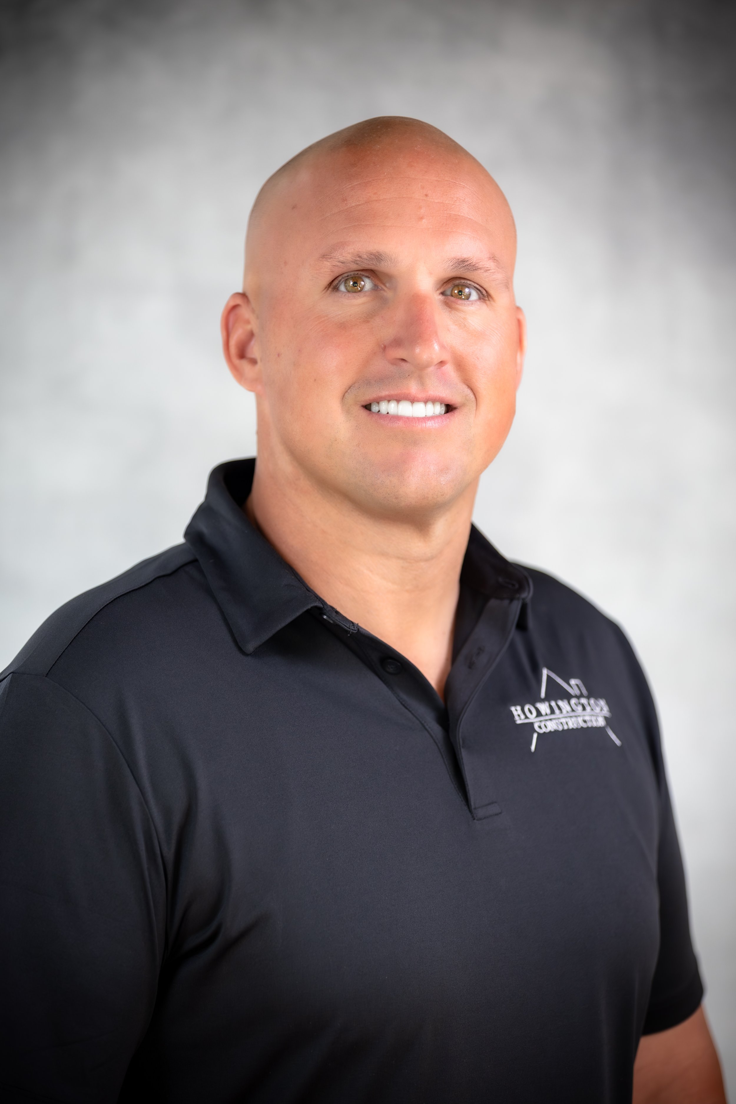 A smiling man in a black polo shirt with 'Howington Construction' logo, standing in front of a white background.