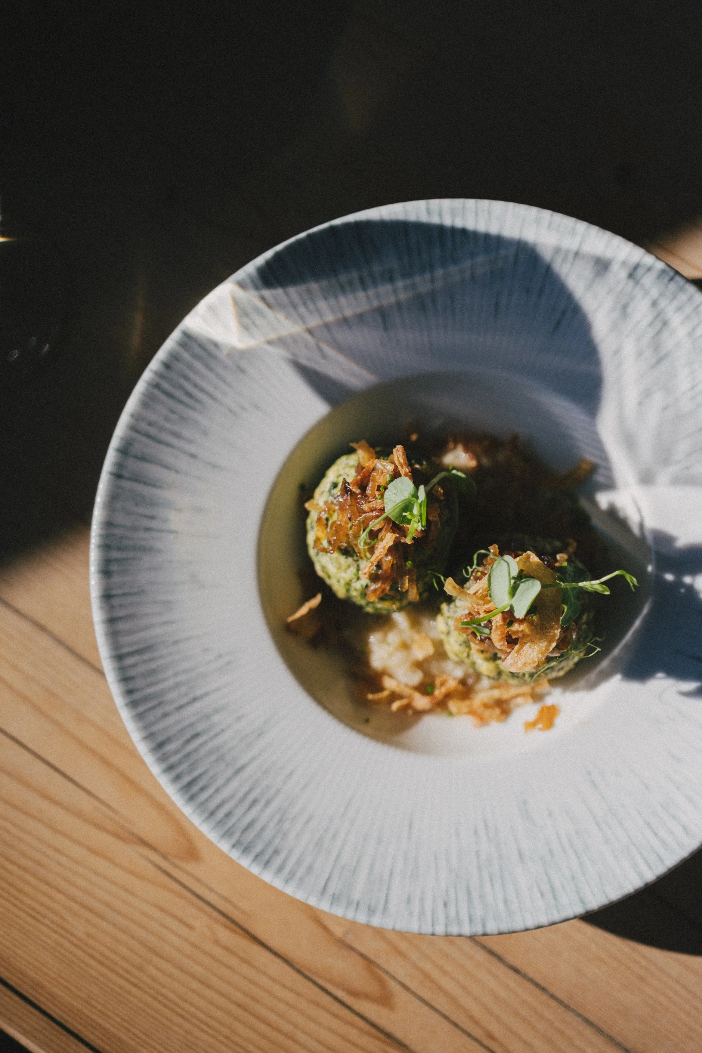 Dreierlei grüner Ball mit Kräutern und Zwiebeln in einer weißen Schüssel, serviert auf einem Holztisch.