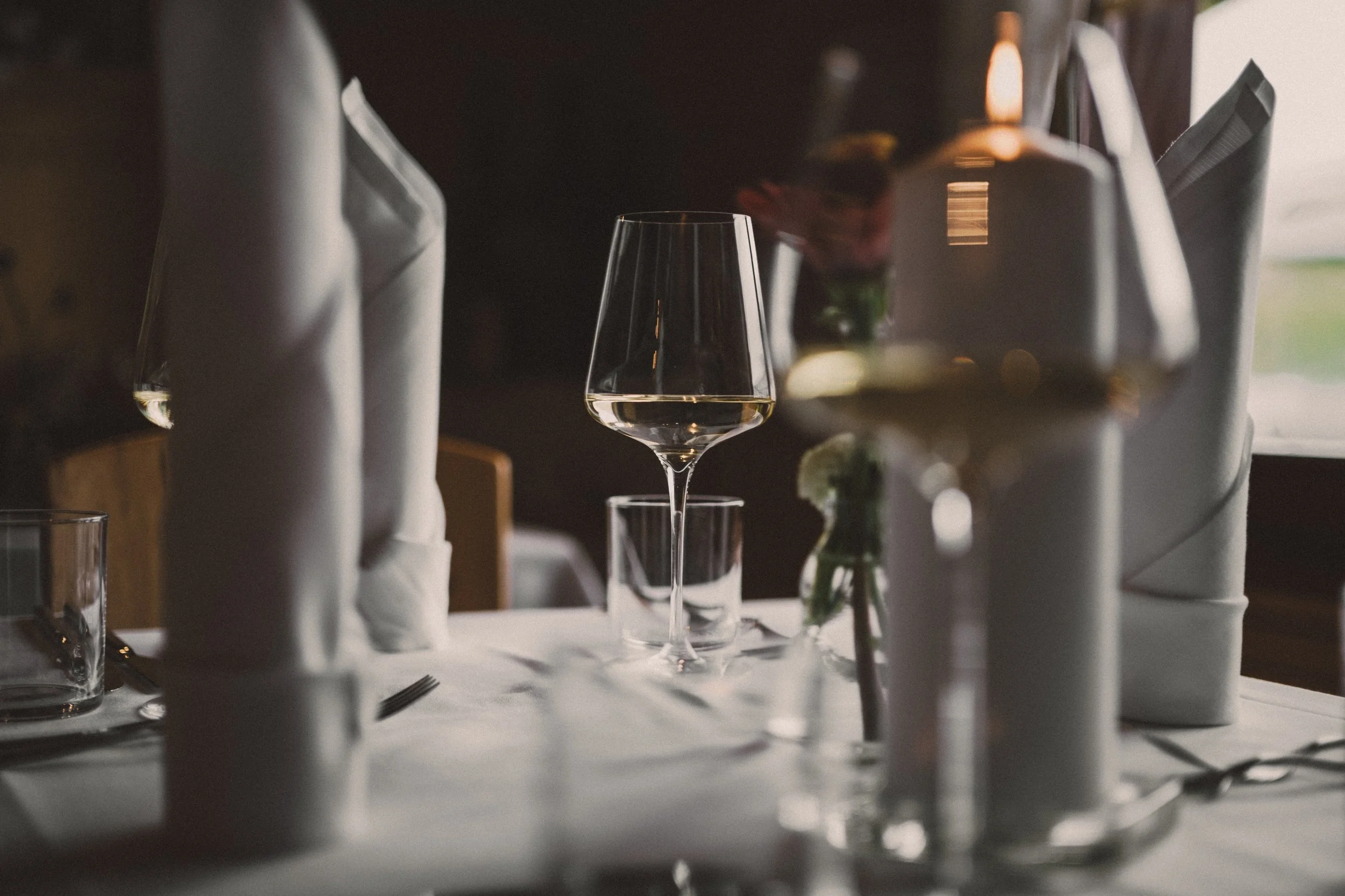 Ein schön gedeckter Esstisch mit einem Weinglas, Wasser, Besteck und Kerzen in einer eleganten Atmosphäre.