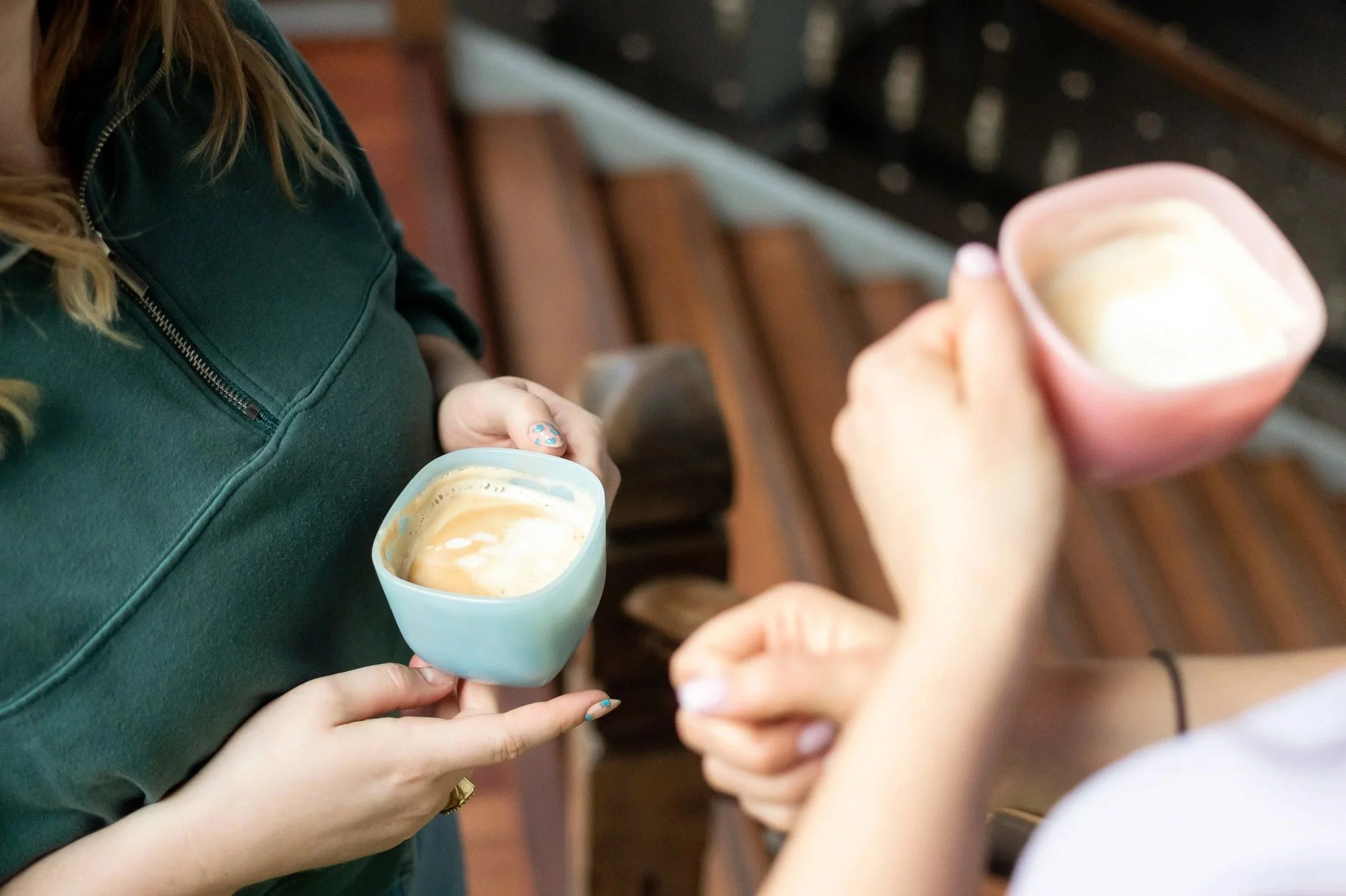 Twee mensen houden elk een kop koffie met schuim, tram of treinbank in de achtergrond.