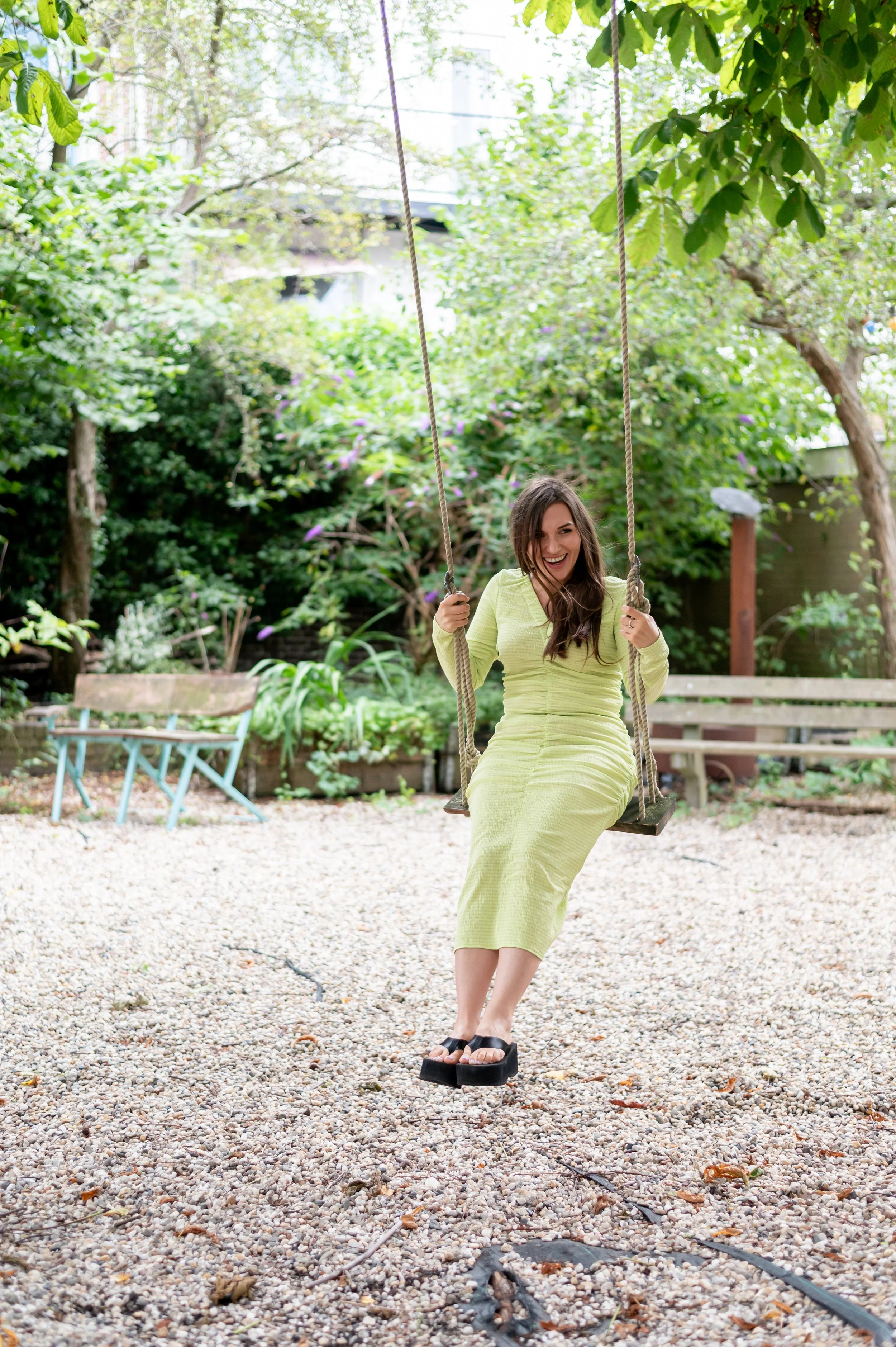Vrolijke vrouw op een schommel in een tuin met groen loof en bloemrijke struiken.