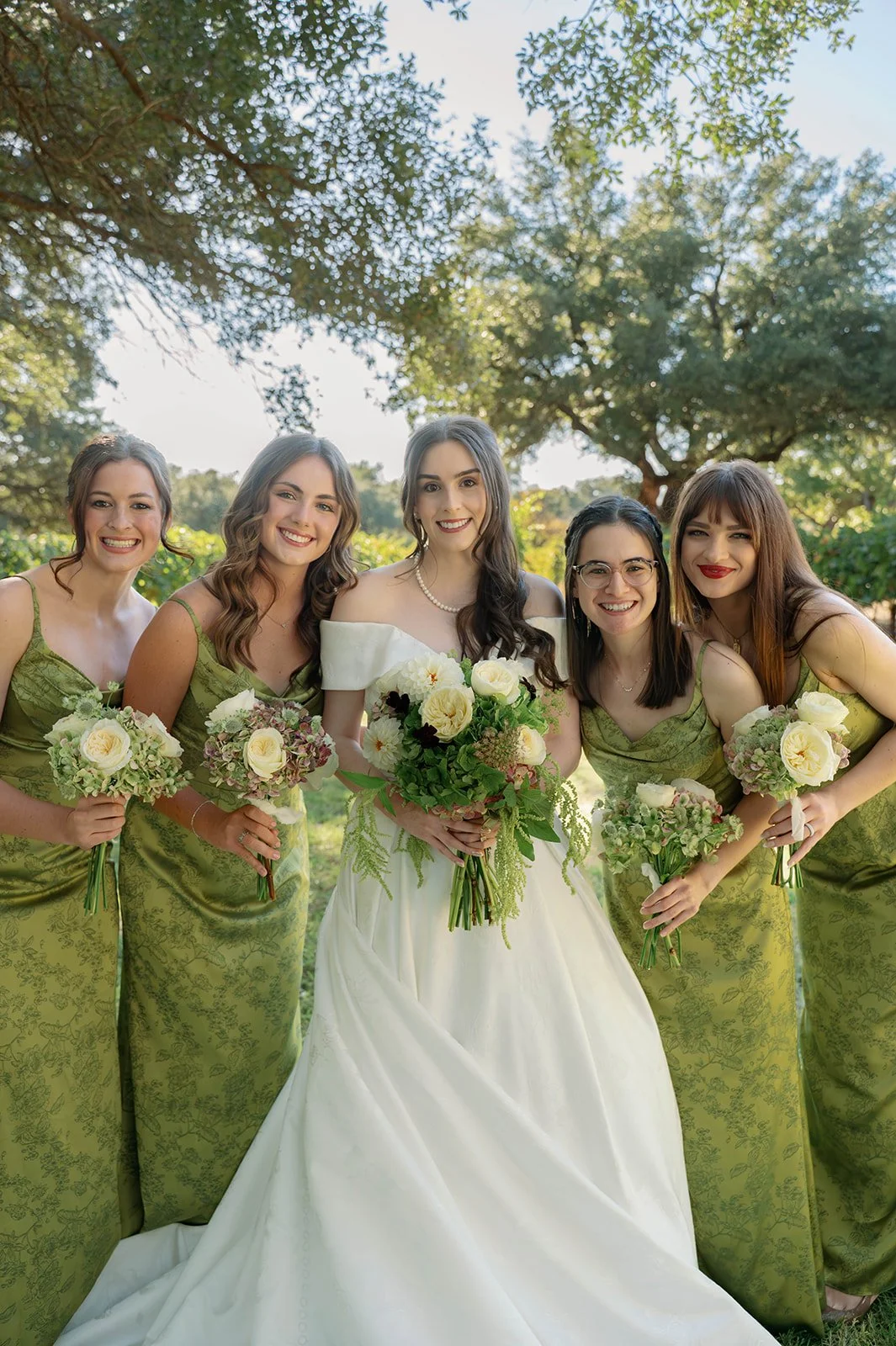 Bride and four bridesmaids holding garden-style wedding bouquets with white roses and greenery designed by Dahlias & Daisies.