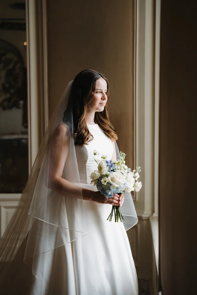 Bride holding a romantic white and pale blue garden-style wedding bouquet designed by Dahlias & Daisies, a San Angelo wedding florist.