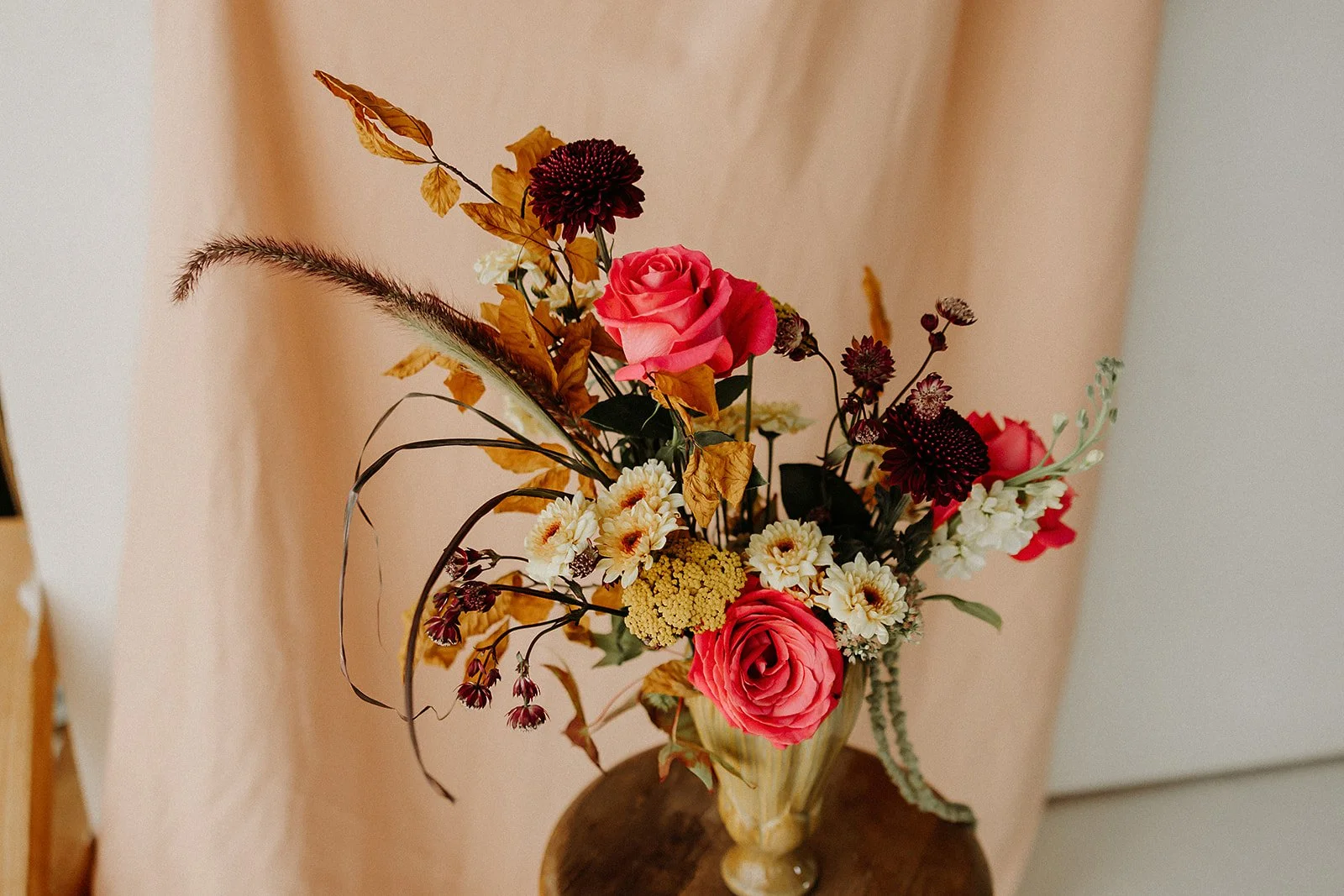 Artistic fall floral arrangement with pink roses, burgundy chrysanthemums, and seasonal foliage by Dahlias & Daisies, San Angelo florist.