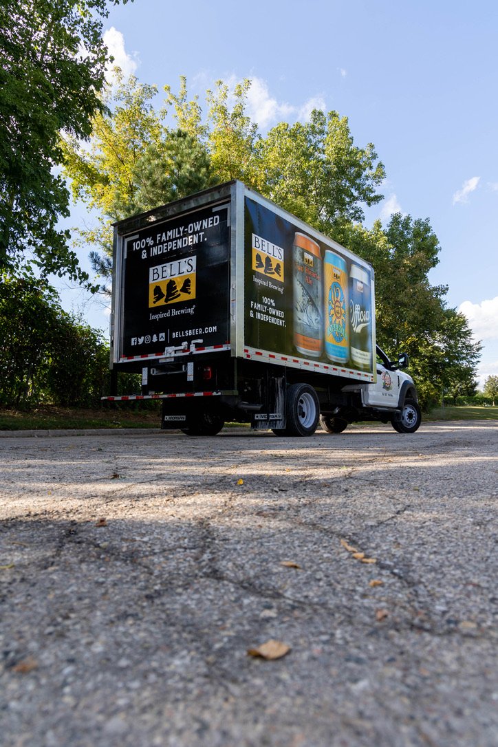 A low angle view of a box truck with a vinyl wrap covering the box that shows different brands of beer