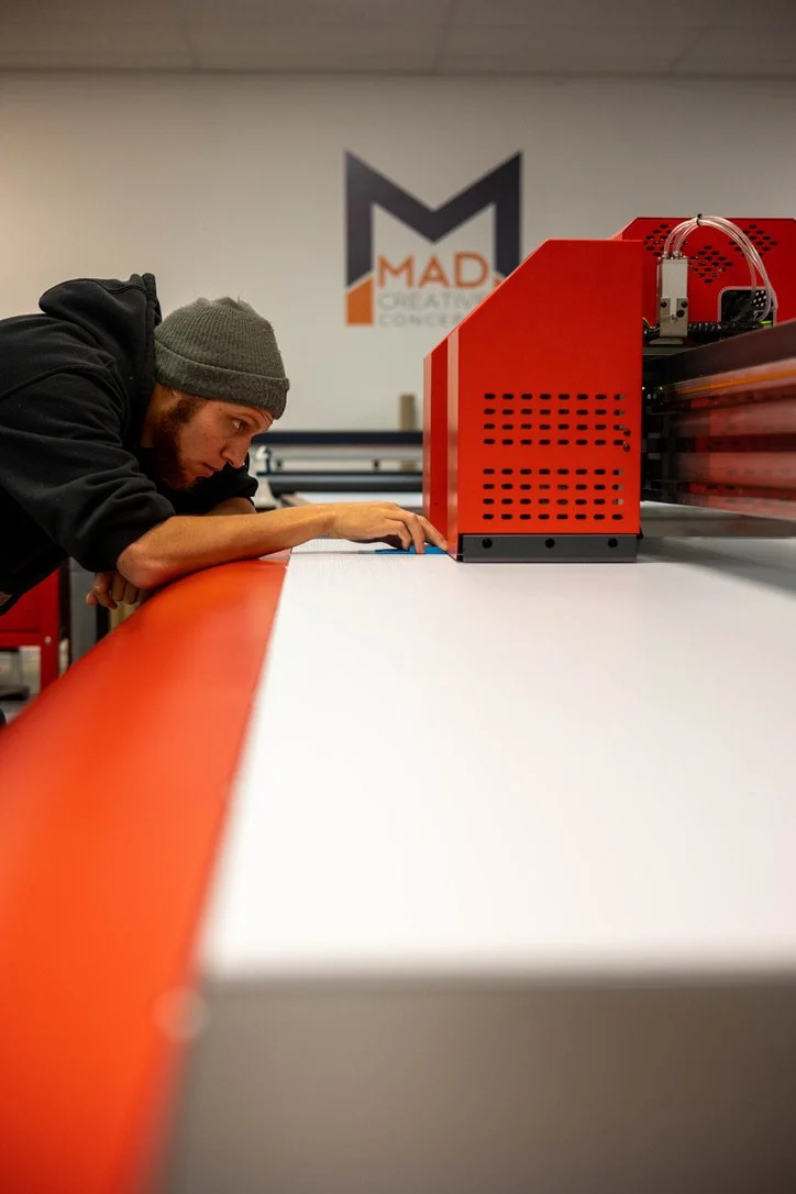 A man in a hat take measurements on an industrial printer