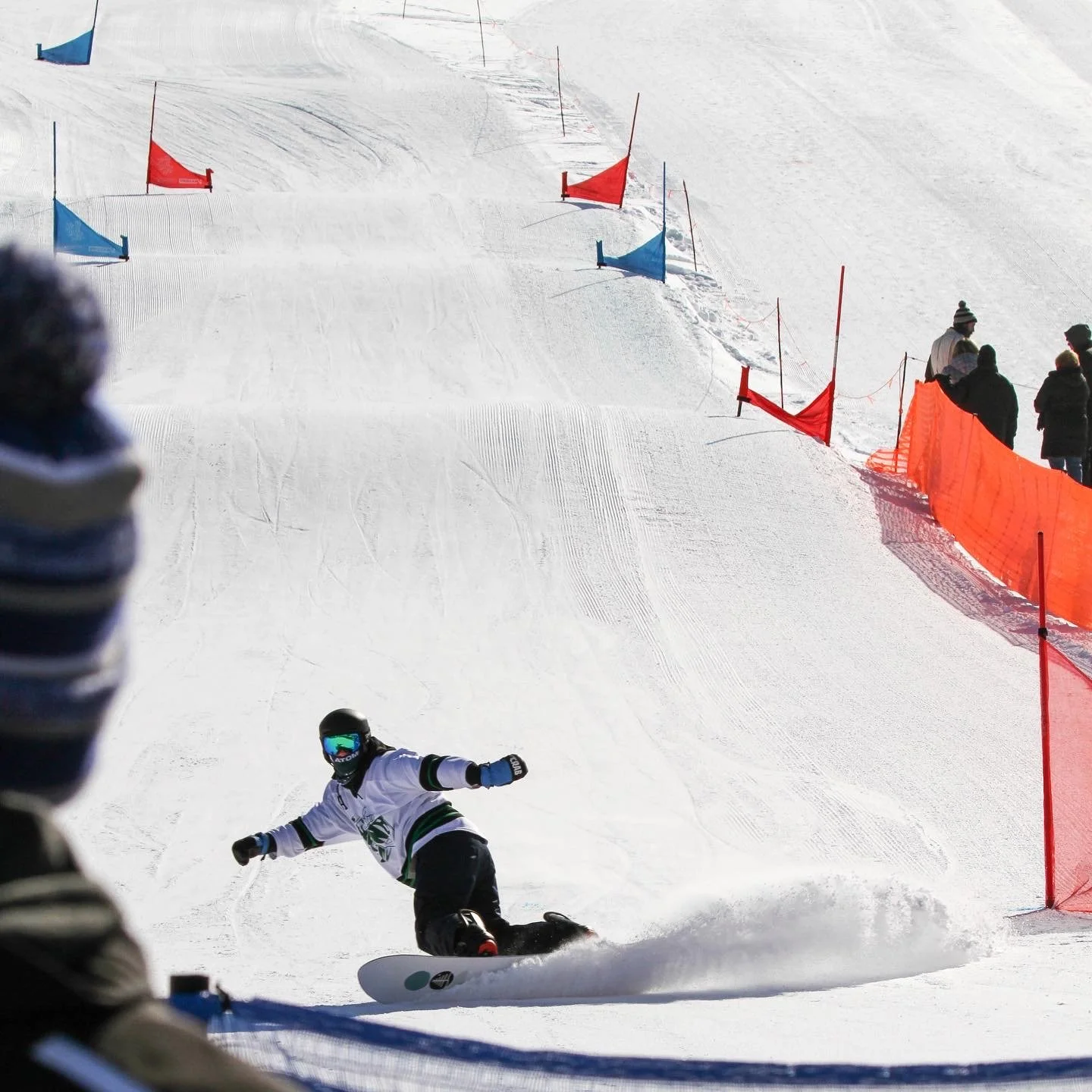 A snowboarder carves a cloud of powder as they screech to a halt from finishing a race