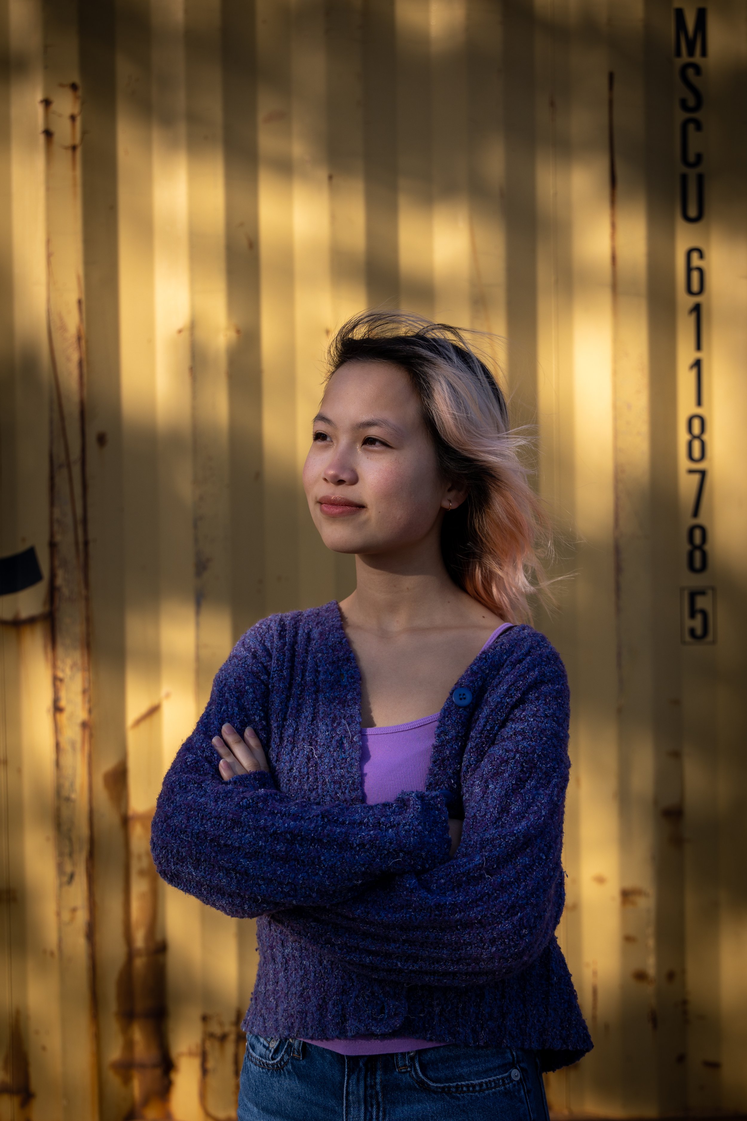 A woman cast in light and shadow poses for the camera in front of a shipping container