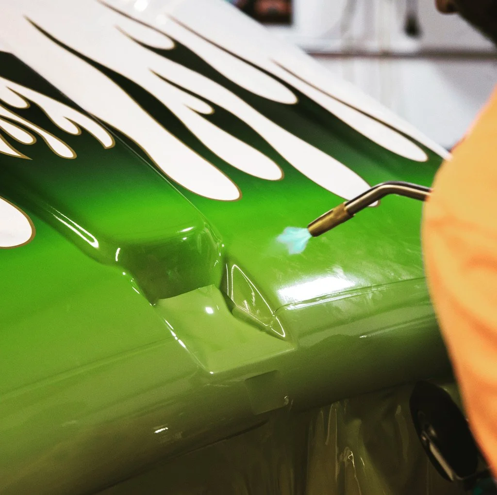 A blow torch blasts fire on a vinyl graphic of green flames onto a truck hood
