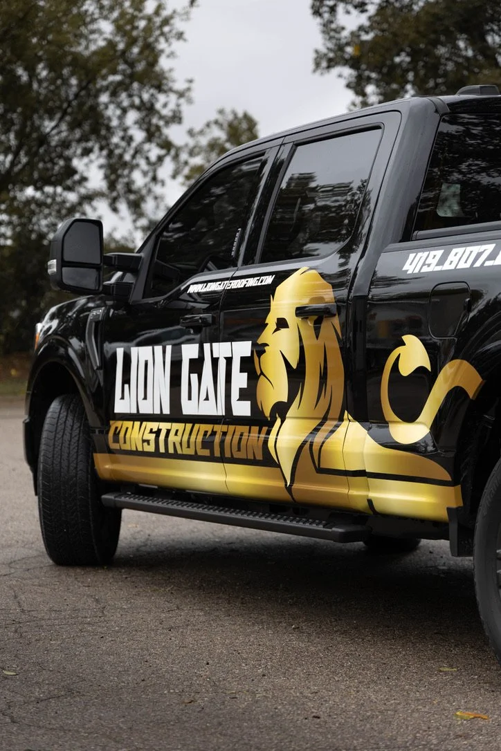 A parked truck has a vinyl wrap on the side that features a lion and the text reads "Lion Gate Construction" 