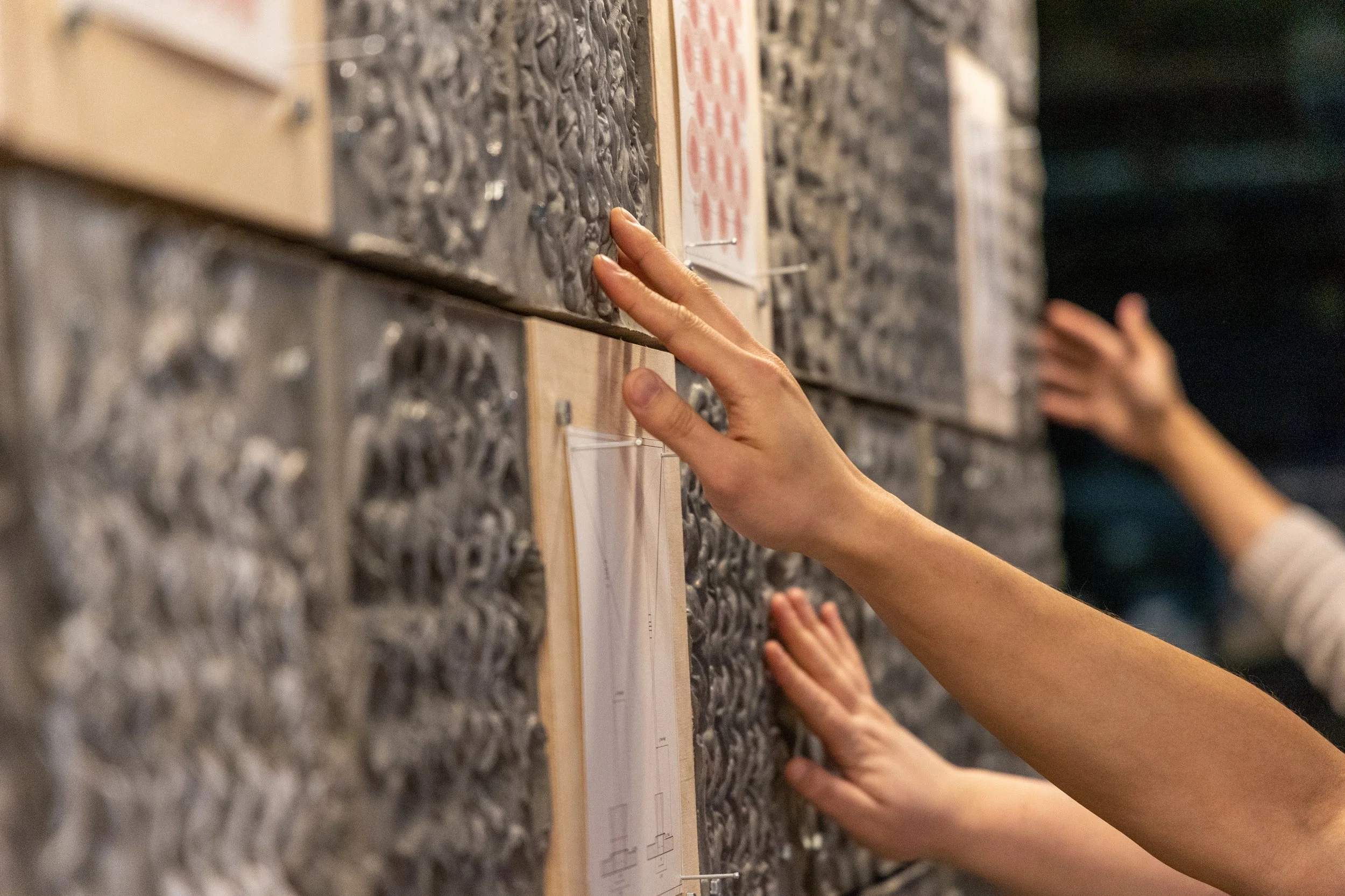 Student hands touch concrete on a wall which is the featured work at a symposium