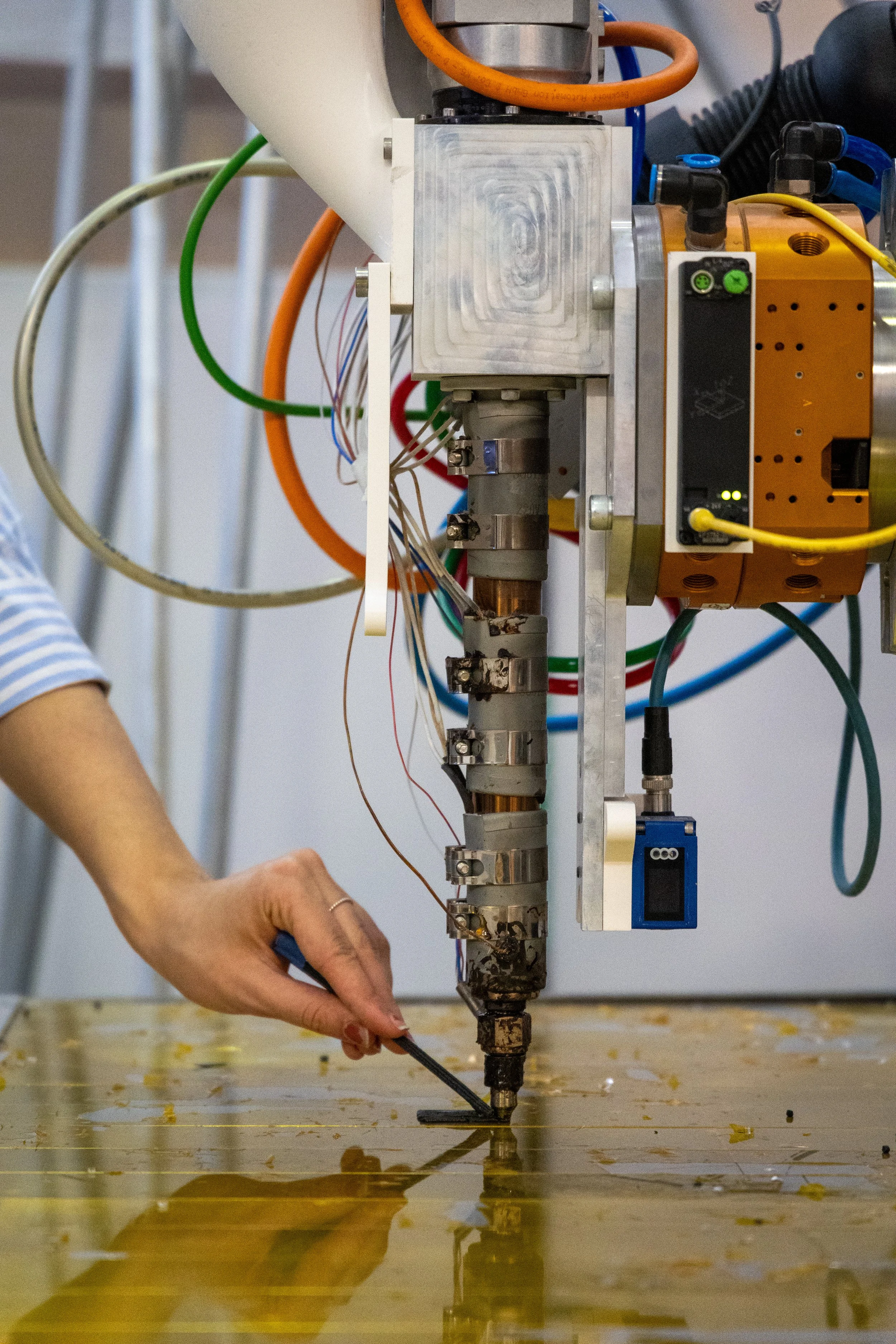 A large industrial robot prints while a hand reaches towards the printing head