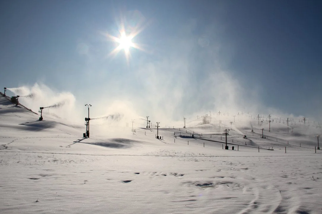A panoramic shot of a ski resort running snow machines under blue sky