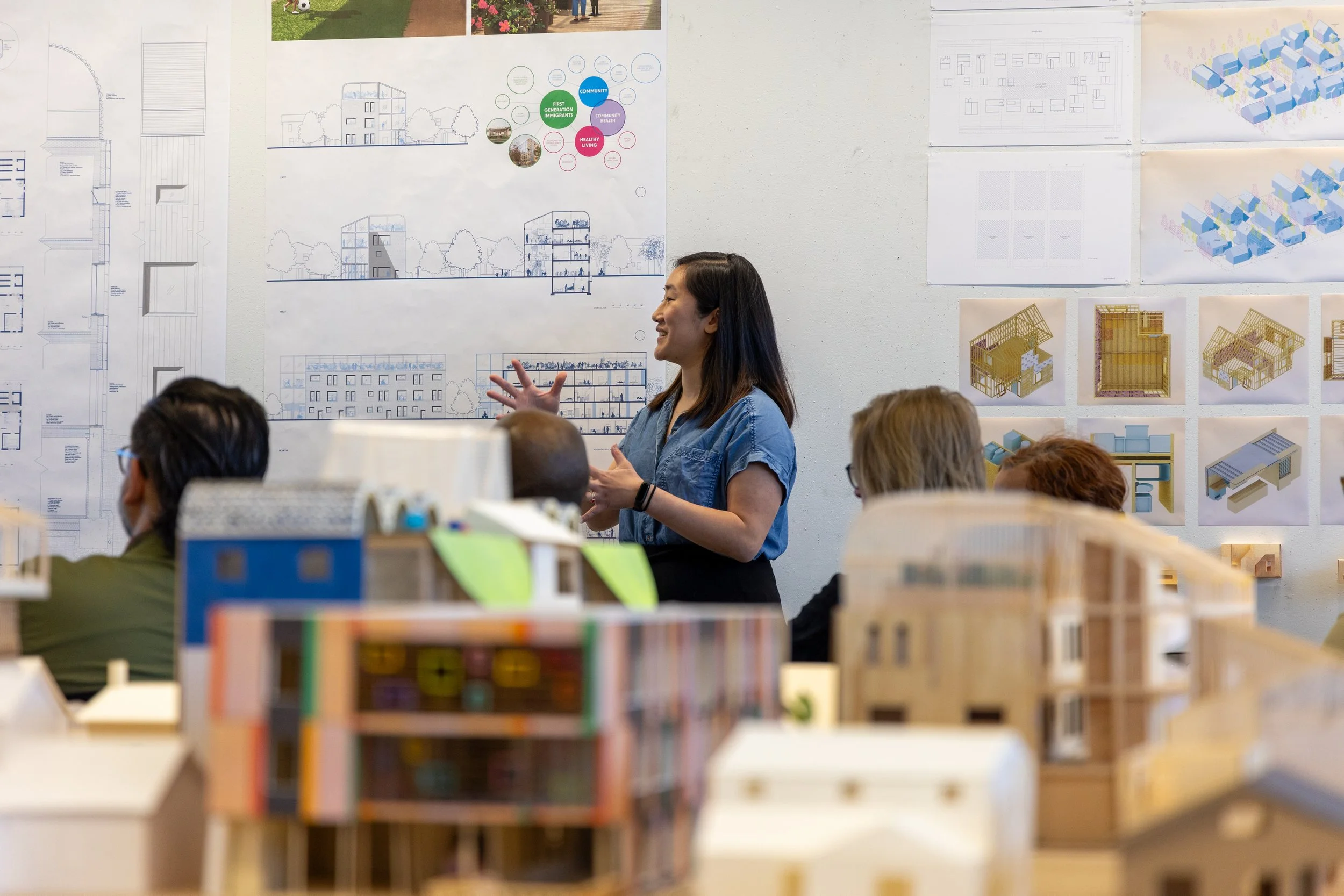 A woman presents her architecture work with slightly blurry models being shown in the foreground