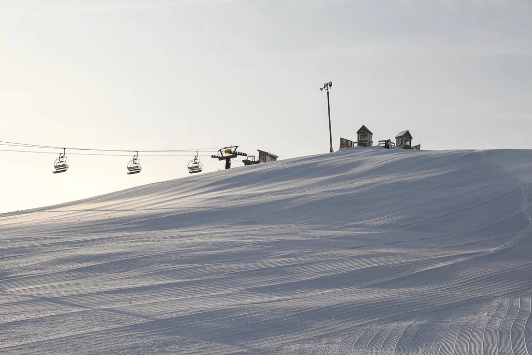 A groomed ski run at sunrise with a chairlift in the distance