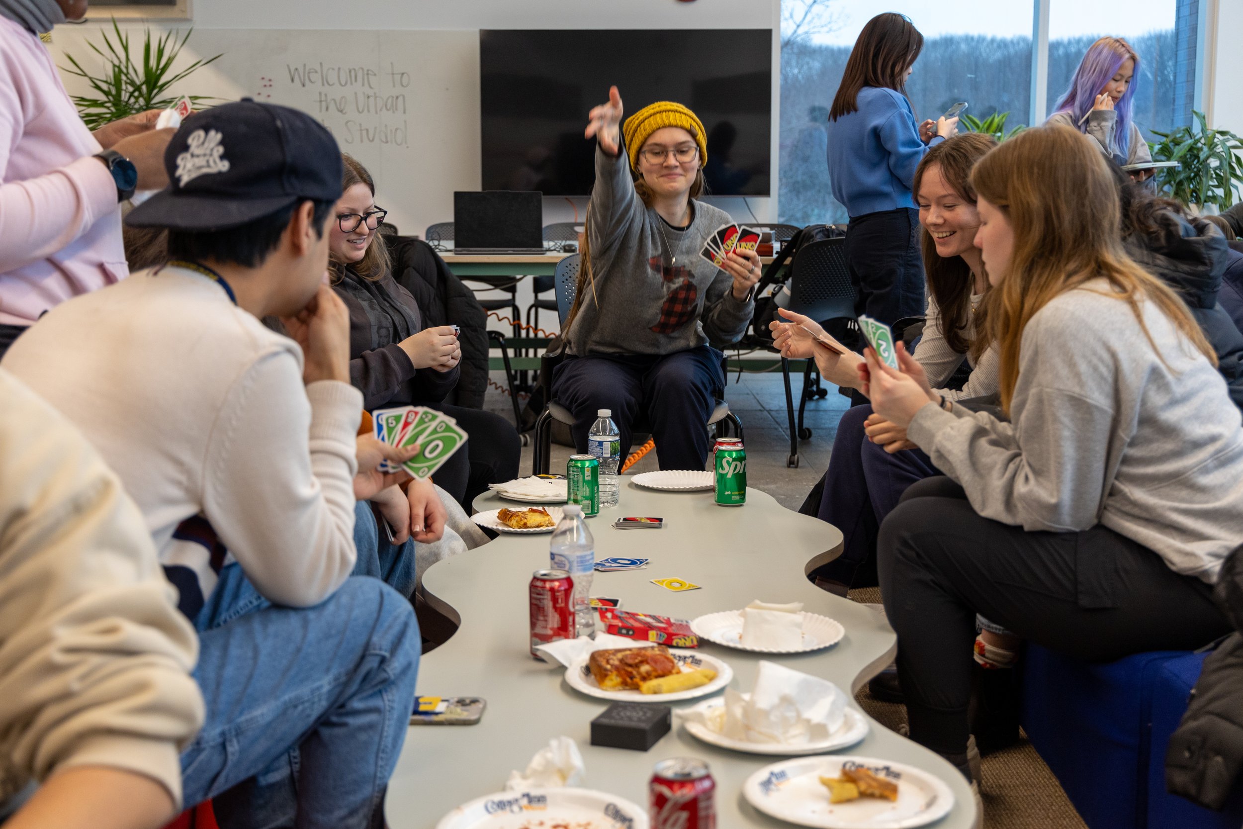 Students play a game of Uno with one woman, center frame, makes a large gesture when playing her card