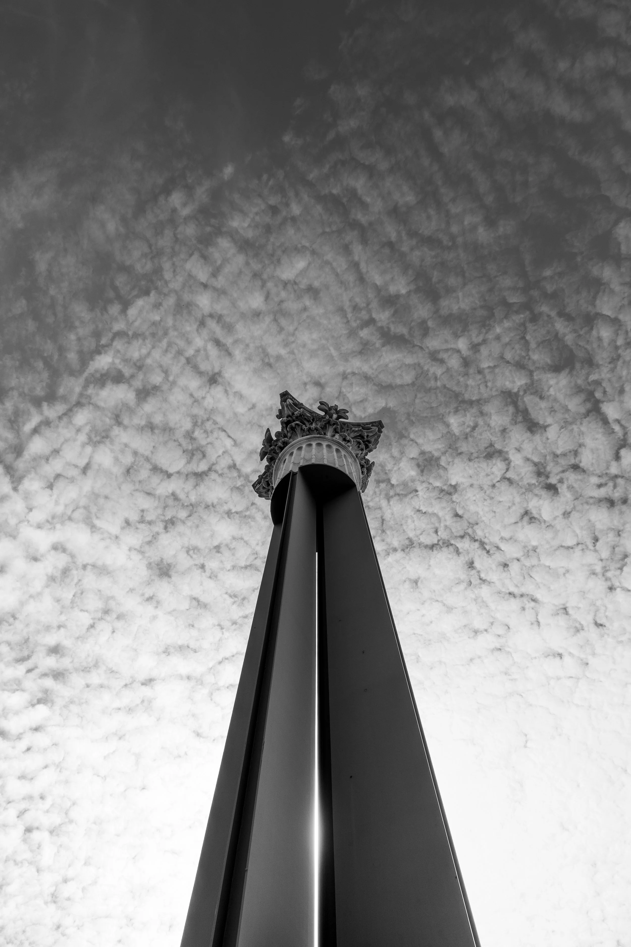 A black and white low angle shot of a metal column with a detailed top