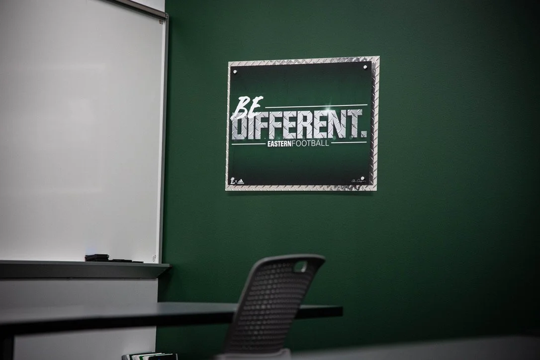 A sign on a green wall in a classroom that says "Be Different"