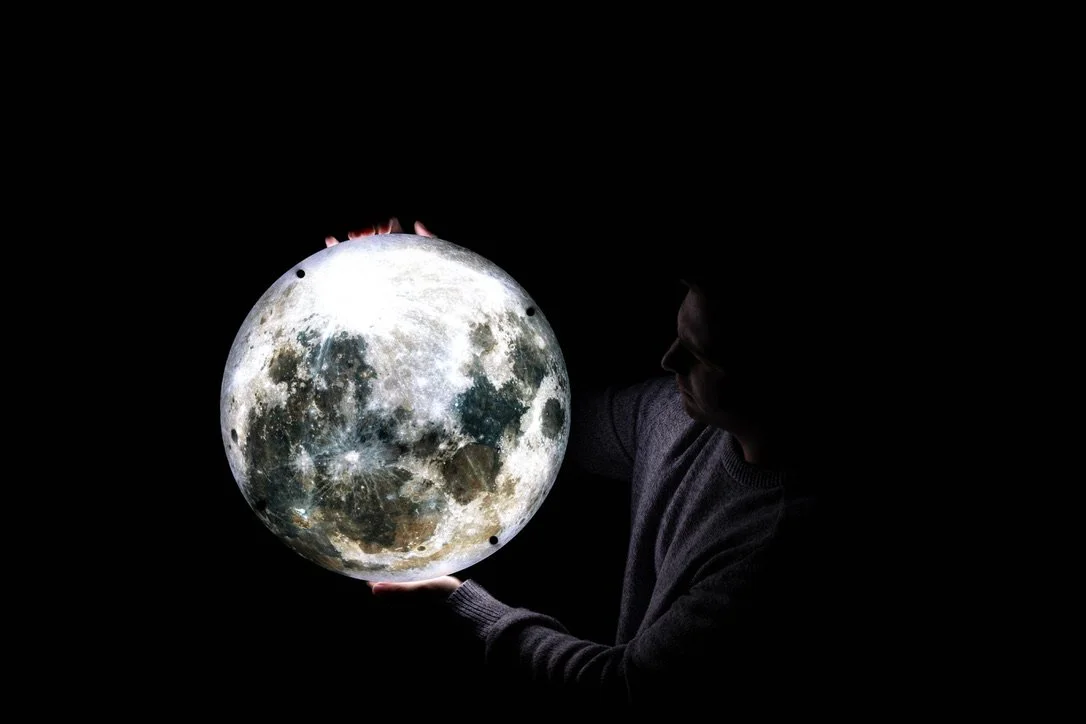 A man hold up an illuminated moon LED sign in the dark