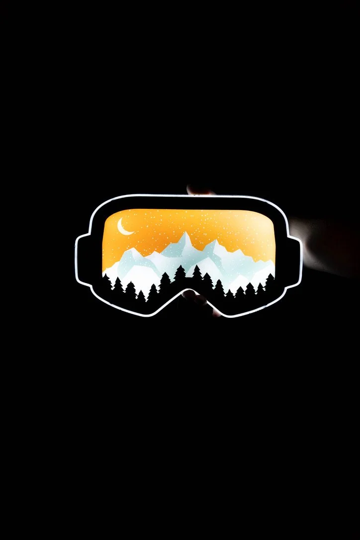 An illuminated pair of ski goggles LED sign being held by a hand in the dark 