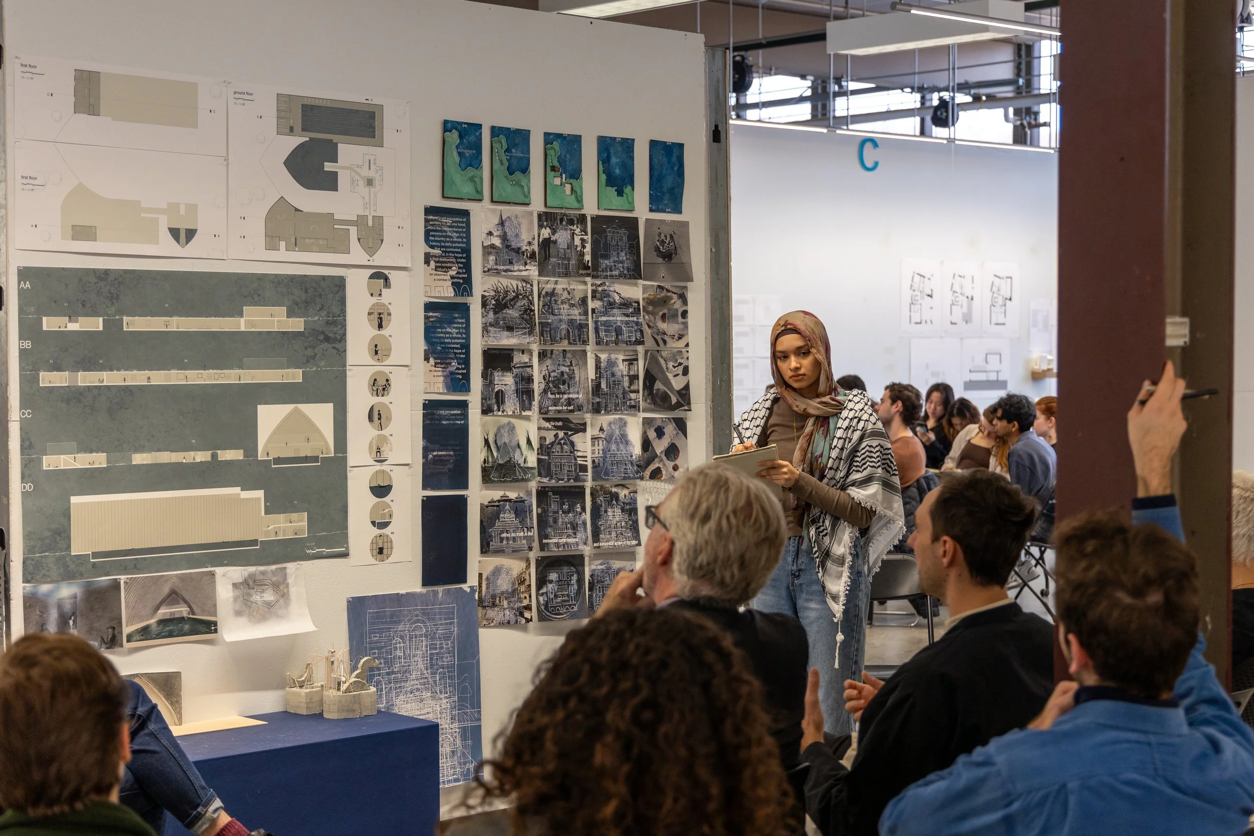 A student listens while they present their work in front of peers and faculty