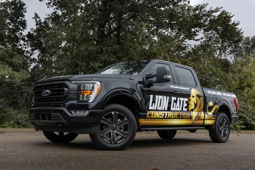 A parked truck has a vinyl wrap on the side that features a lion and the text reads "Lion Gate Construction" 