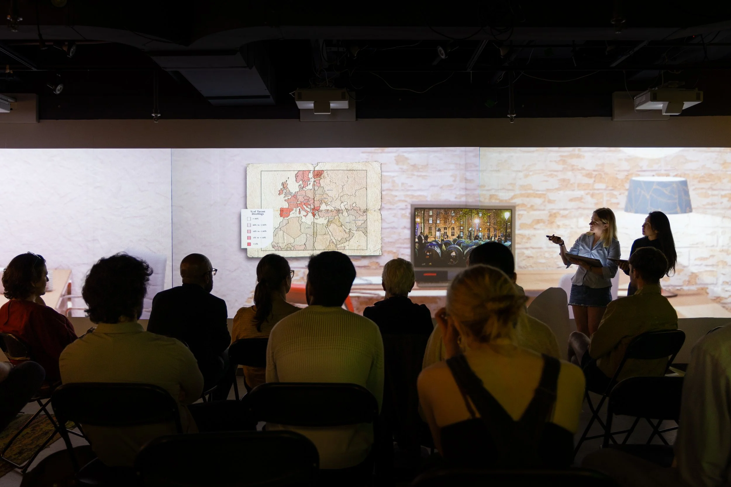 Two student present their work on a large projector in front of a row of peers and judges