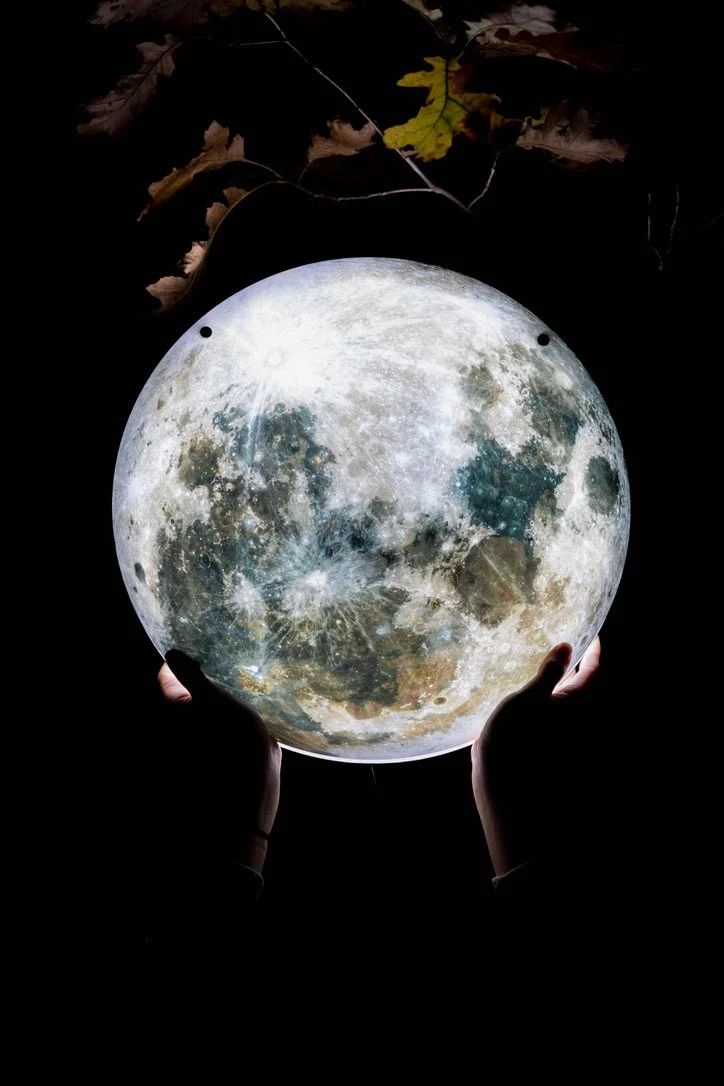 A pair of hands hold up an illuminated moon LED sign in the dark