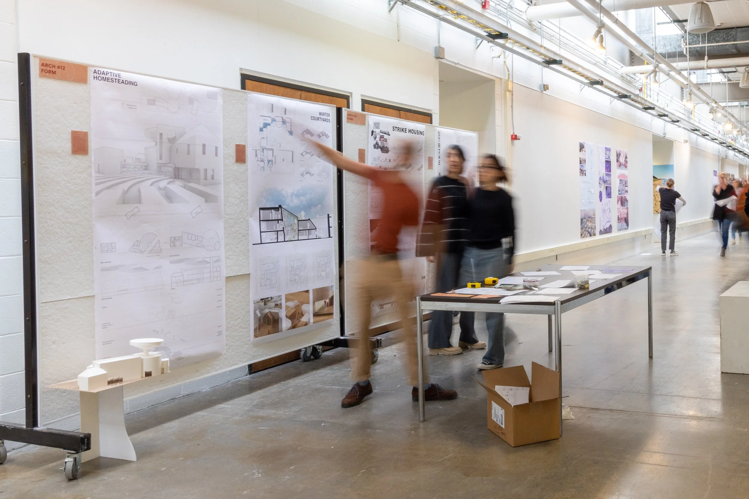 Blurry students discussing pinned up architecture work in a building
