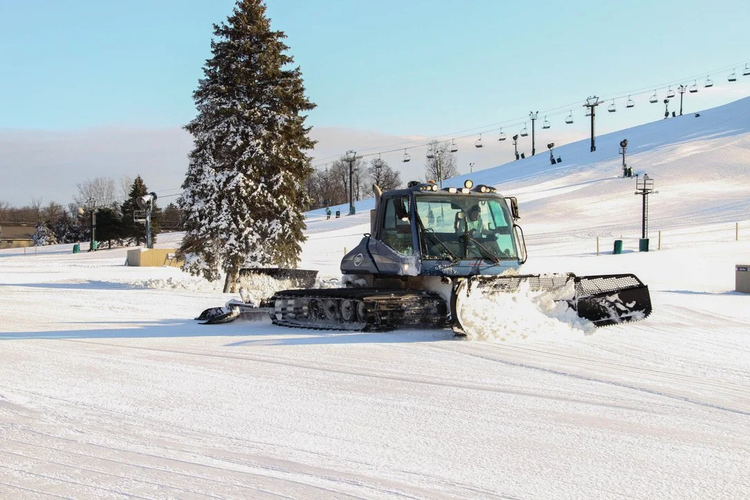 A snowcat pushes snow at the base of a mountain resort