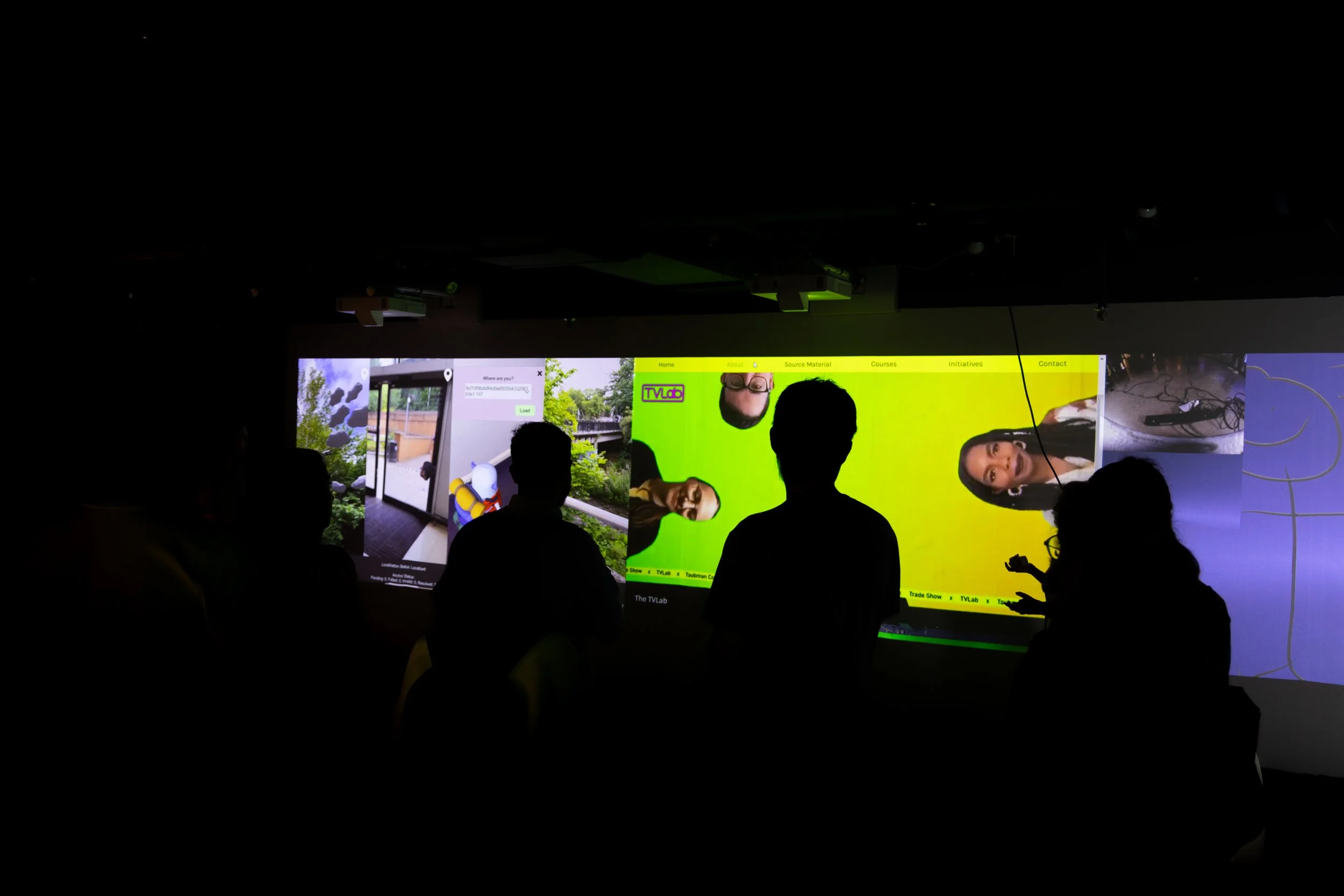 Silhouettes of people standing in front of a screen with green-screen people looking at them