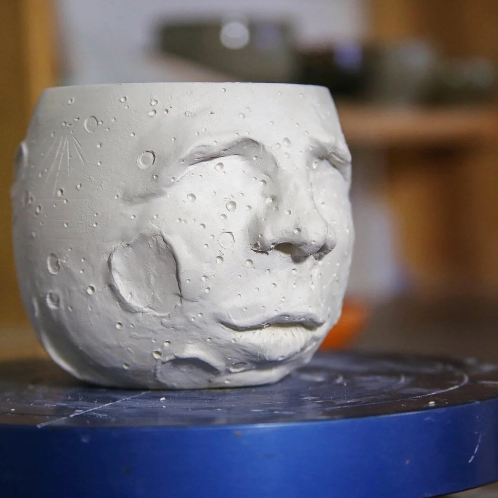 A clay cup in the shape of the moon with a face on it