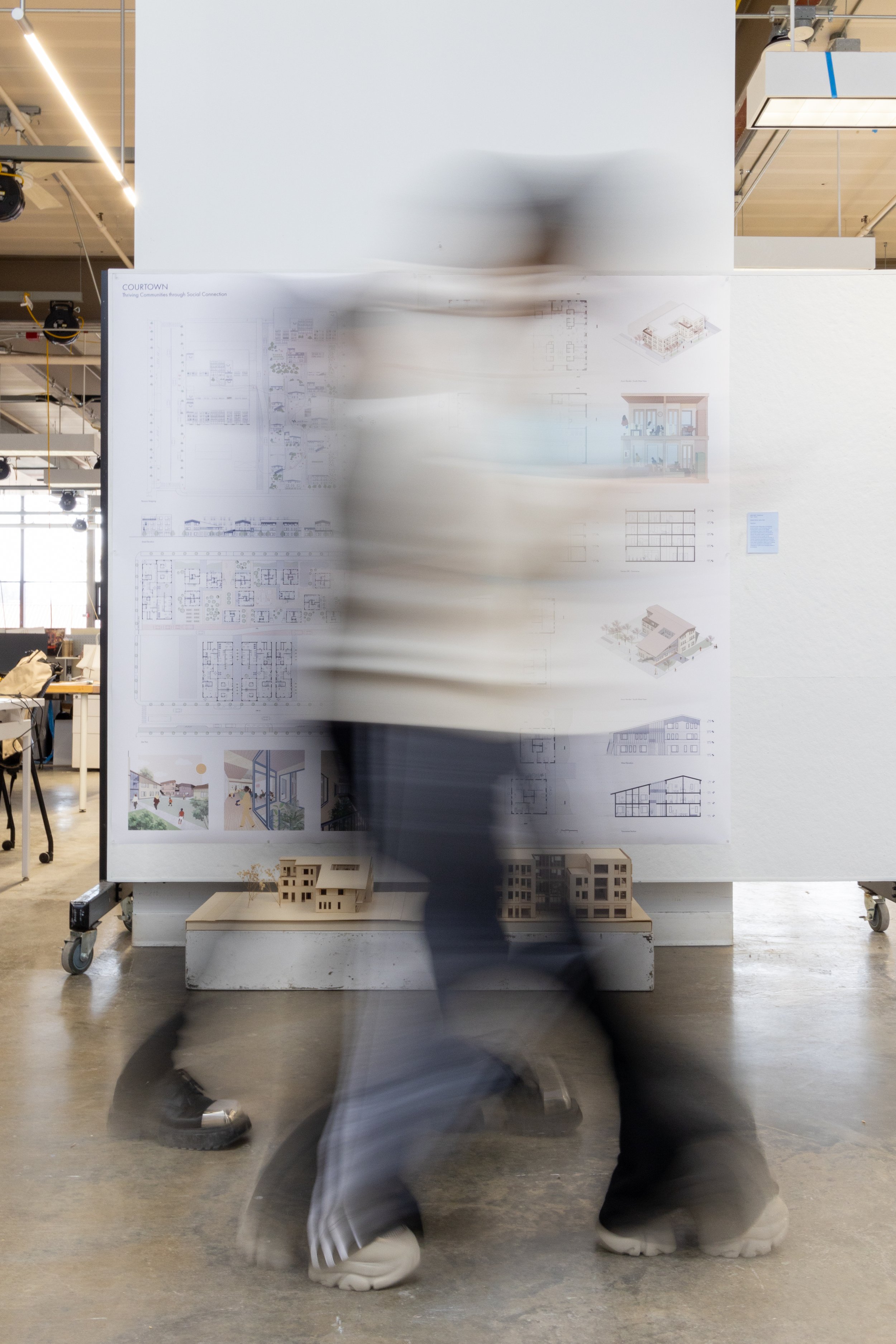 A blurry figure walks in front of architecture models placed in a hallway