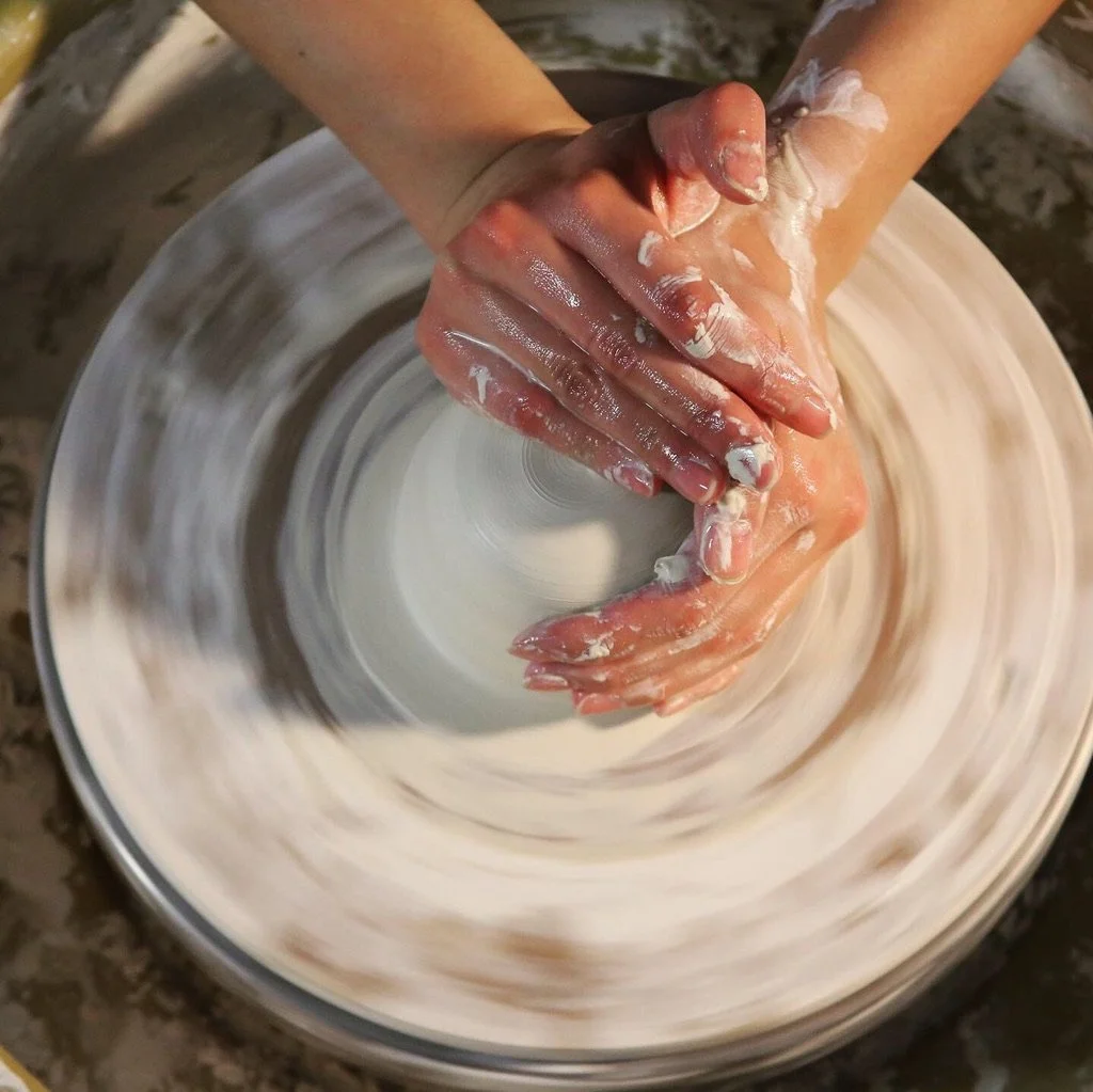 A pair of hands work with clay on a throwing wheel