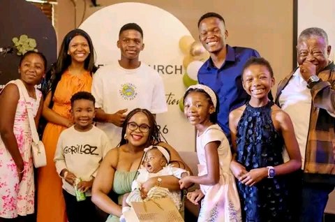 Two people hugging in a room, one wearing glasses and a dark jacket, the other in a light, fuzzy coat.