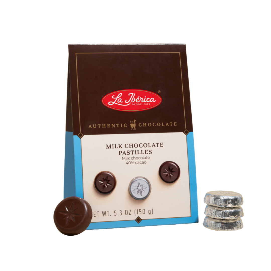 Box of La Iberica milk chocolate pastilles with three unwrapped chocolates nearby, showing chocolate in silver foil wrappers.