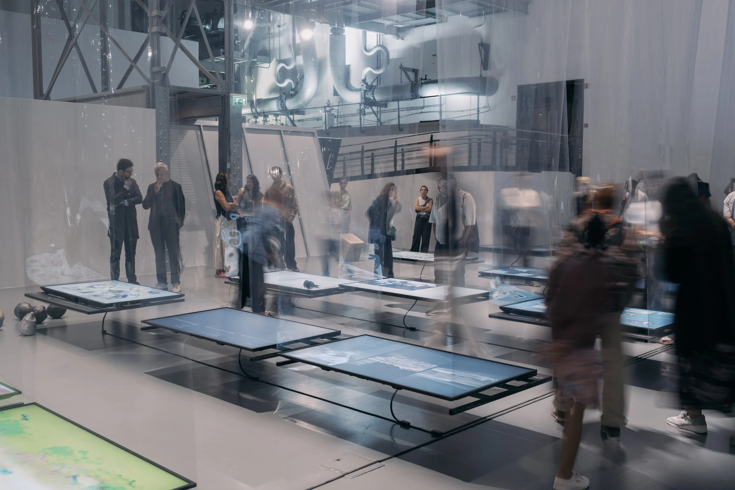 People in a gallery space looking at suspended horizontal screens showing films.