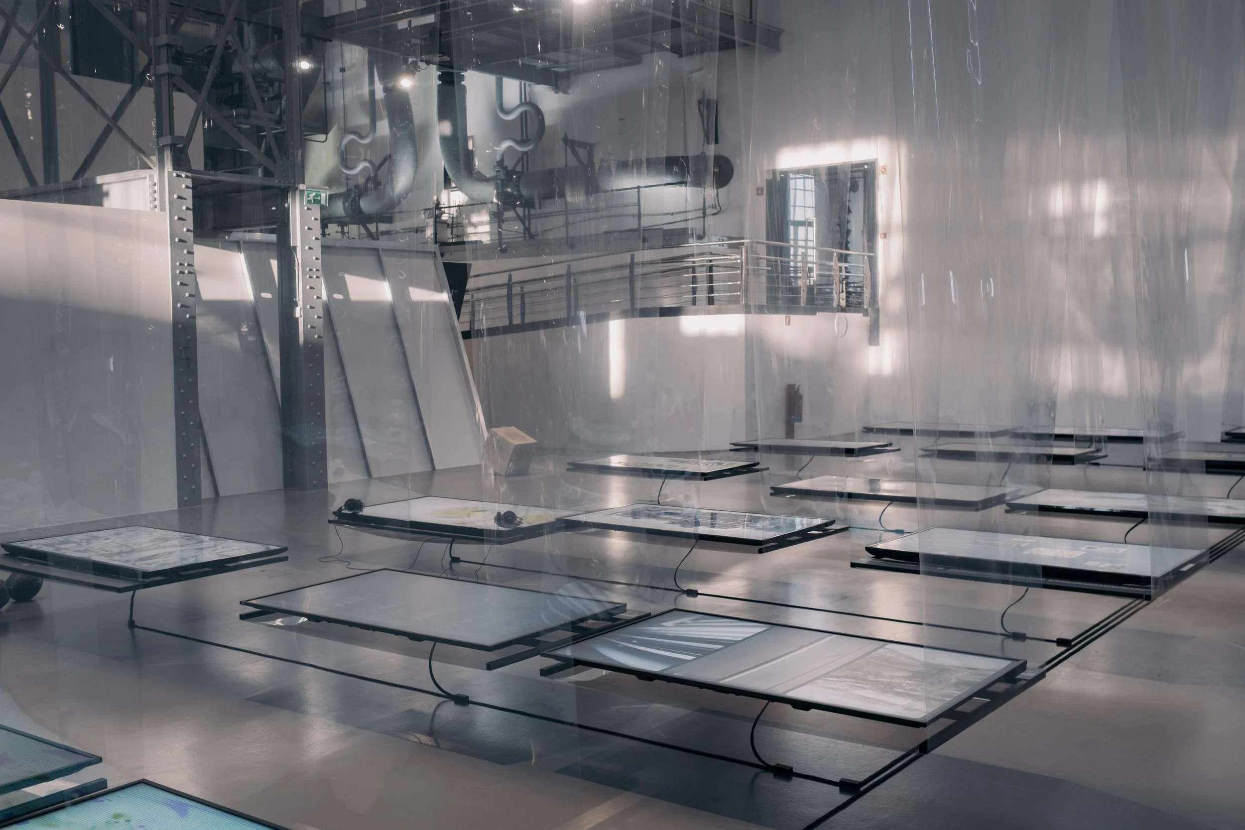 Horizontal TV screens suspended from sheets of plastic in a gallery space.